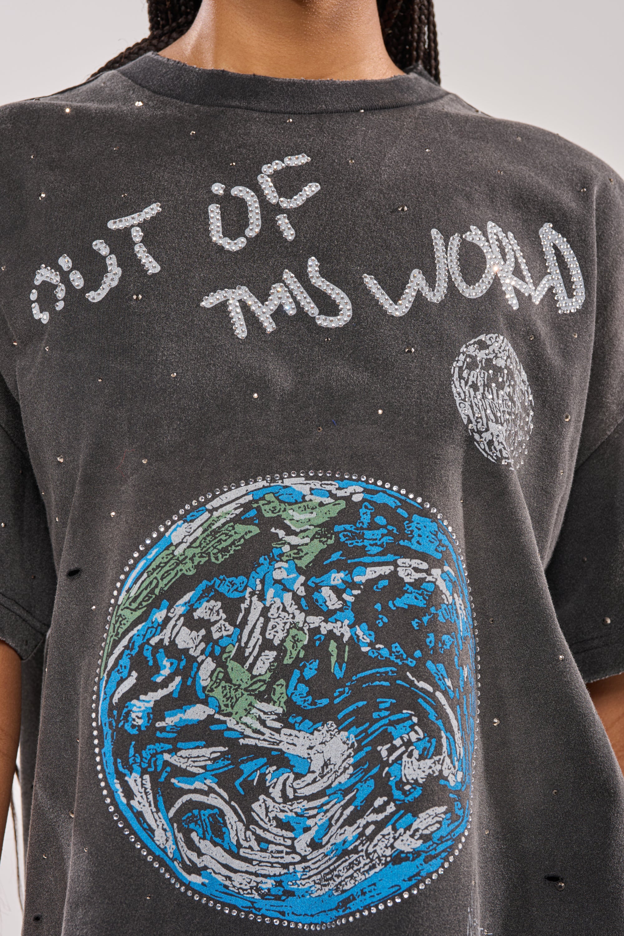 A person wears the OUT OF THIS WORLD GRAPHIC TEE, a black, space-inspired shirt with white speckles, an Earth graphic, and "OUT OF THIS WORLD" in a handwritten style above. 6
