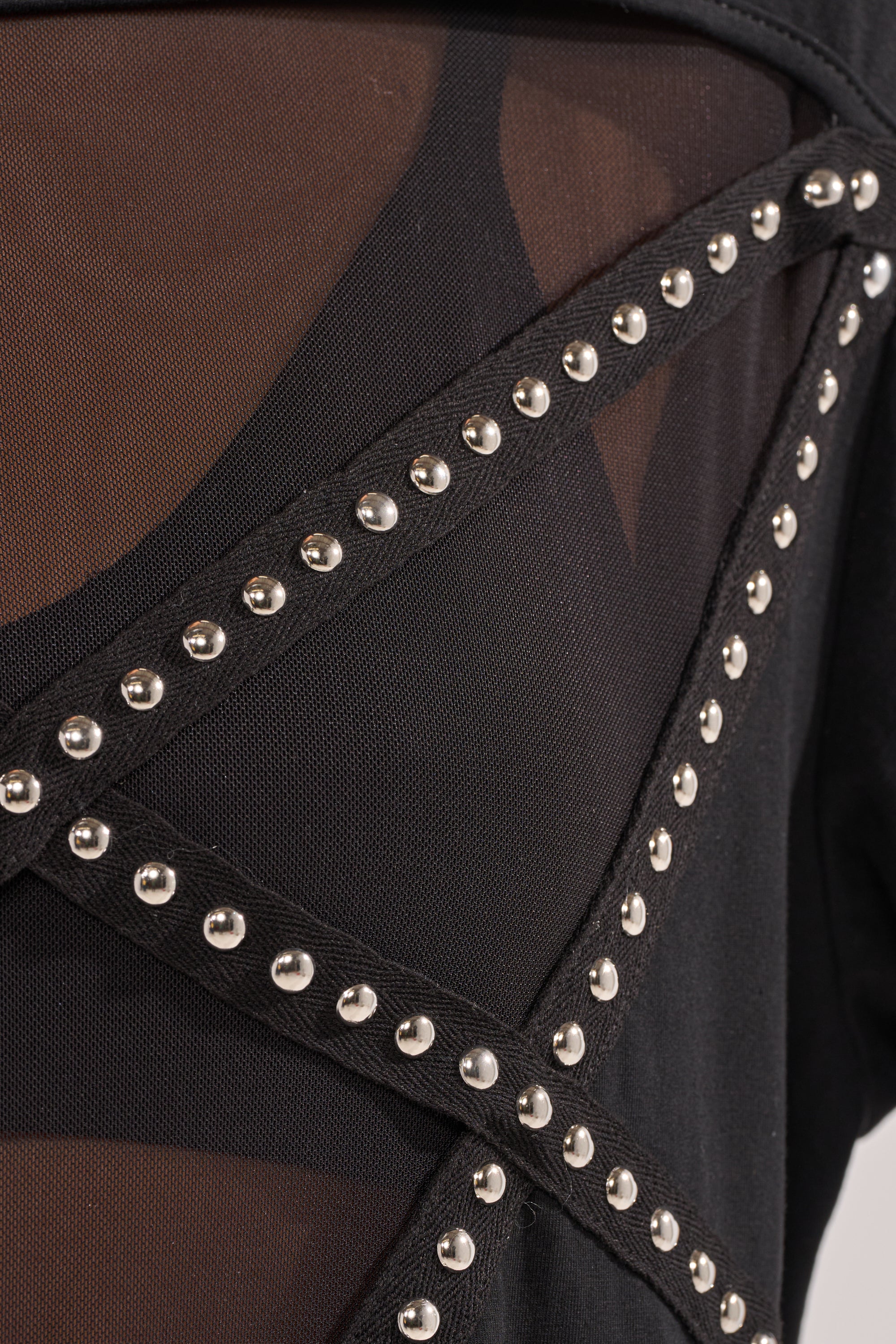 Close-up of the MISTA RAJ OVERSIZED TEE in black mesh, featuring intersecting straps and silver studs over sheer paneling—a modern, streetwear-inspired detail. 6