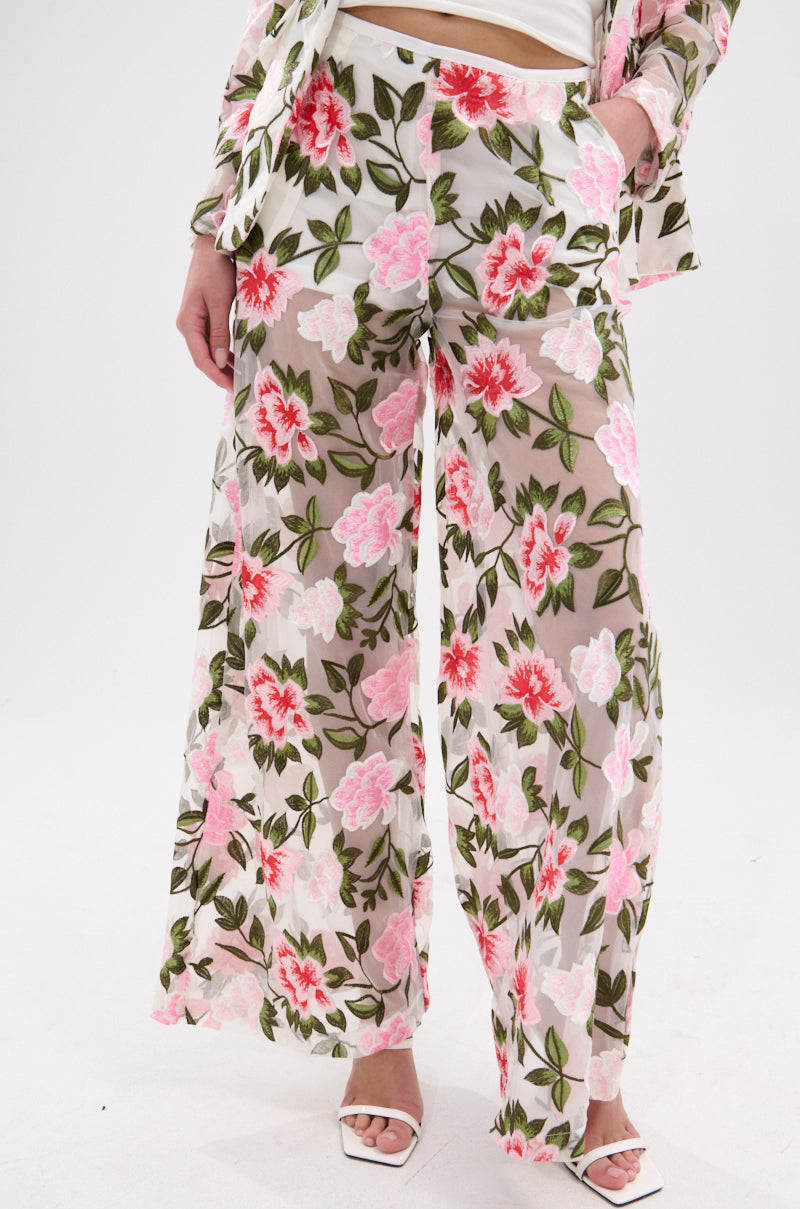 A person models BLOSSOM LACE PALAZZO PANTS featuring a wide-leg silhouette and pink-red floral lace embroidery, styled with a matching top and white open-toe heels, standing against a plain white background.