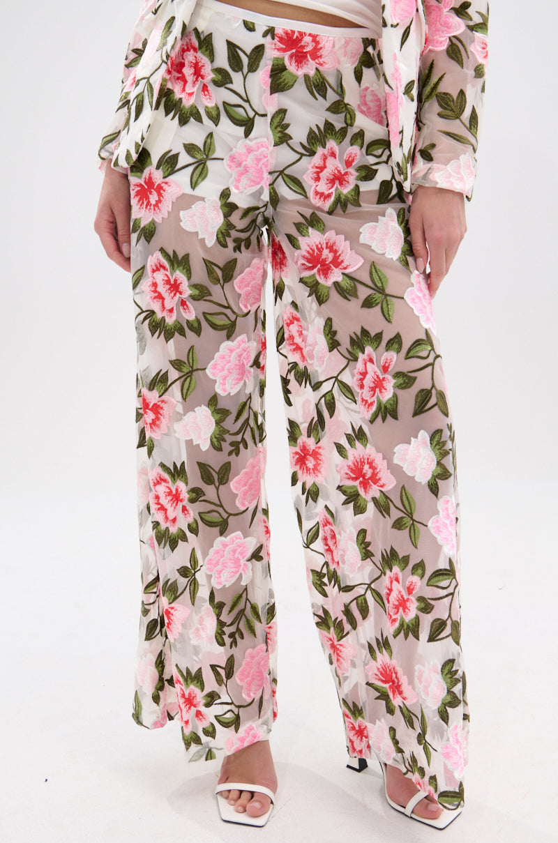 Wearing BLOSSOM LACE PALAZZO PANTS with a wide leg and floral lace embroidery, paired with a matching floral jacket and white open-toe heels, the model stands against a plain white background.