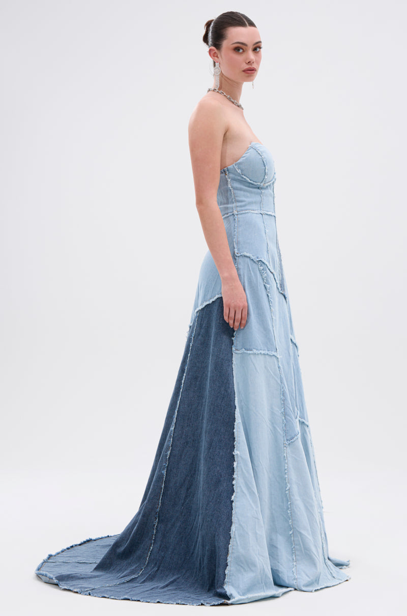A woman in profile showcases the IT'S BRITNEY PATCHWORK DENIM MAXI DRESS, a strapless maxi with patchwork detailing and a mermaid skirt. She wears her hair in a bun, accessorized with earrings and a choker, set against a plain background.