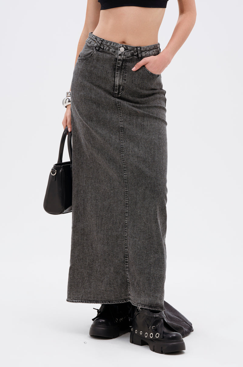 A person wears the OH THE DRAMA DENIM MAXI SKIRT WITH TRAIN IN GREY, paired with a black crop top, chunky black boots, and holds a black handbag. One hand is in the skirt pocket. The plain white background highlights the look.