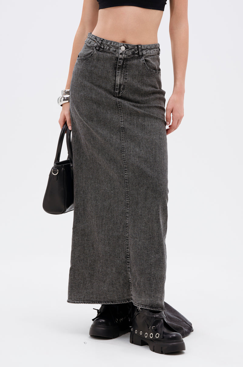 A person wears the OH THE DRAMA DENIM MAXI SKIRT WITH TRAIN IN GREY—high rise, faded black-grey with a raw hem—paired with a black crop top, chunky boots, bracelets, and a black handbag. The background is plain white.