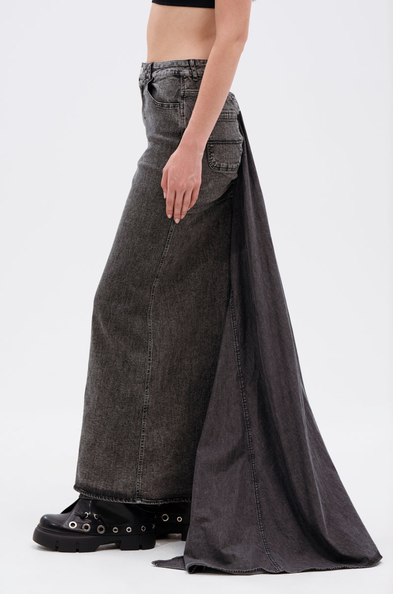 A person in the OH THE DRAMA DENIM MAXI SKIRT WITH TRAIN IN GREY, featuring a ruched back and draped panel, styled with chunky black shoes and a black crop top, shown from the side against a plain background.