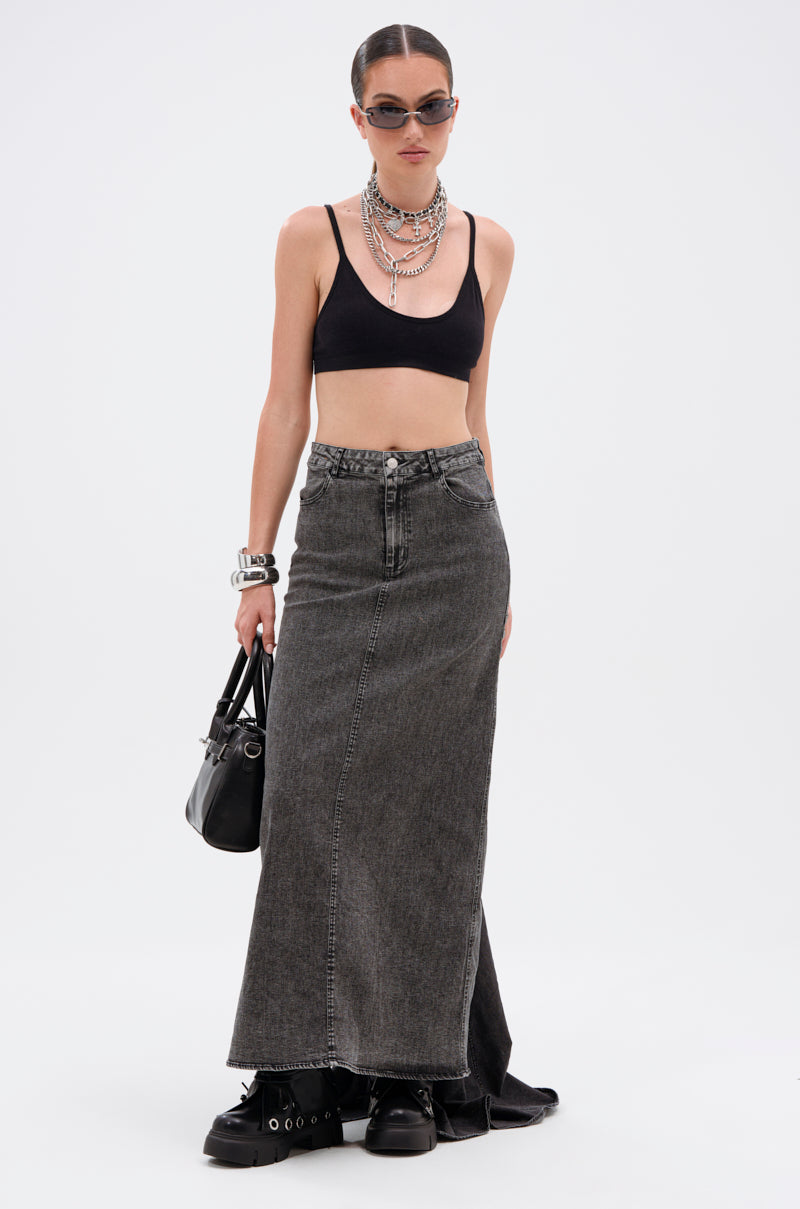 A woman in sunglasses and layered silver necklaces wears a black crop top, chunky black shoes, and holds a black handbag, paired with the OH THE DRAMA DENIM MAXI SKIRT WITH TRAIN IN GREY, standing against a plain white background.
