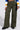 A person wearing IT IS BACK CARGO PANTS in olive green, featuring a high-rise waist, wide legs, and ribbon details, paired with a colorful long-sleeve top. Black platform boots and a matching handbag complete the ensemble.