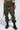 Someone wearing IT IS BACK CARGO PANTS, featuring olive-green color, adjustable drawstring hems, and a high-rise waist, stands against a plain background. They pair the look with black combat boots, a colorful sweatshirt, and a black purse slung over one shoulder.