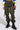 A person wears IT IS BACK CARGO PANTS in olive green with adjustable drawstring hems, black lace-up boots, and carries a sleek black bag. They sport a multicolored long-sleeve top with blue, white, and yellow stripes.