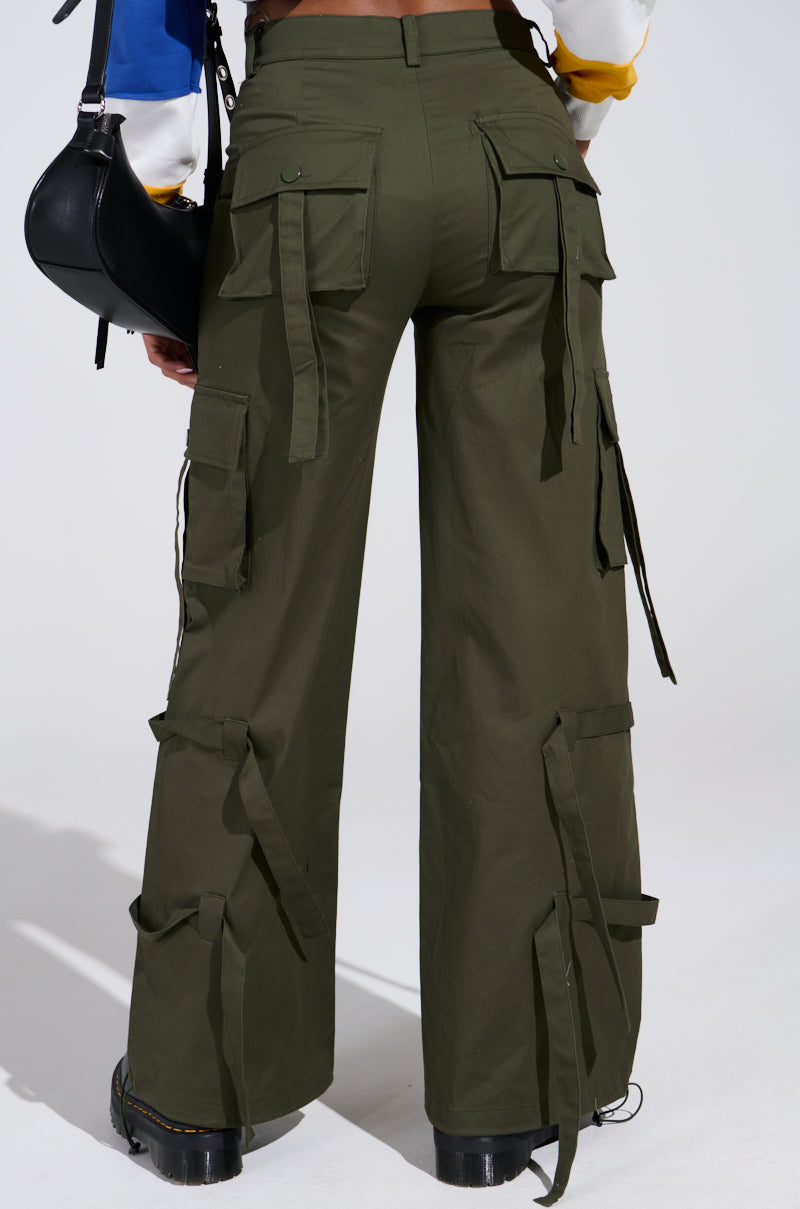Dressed in IT IS BACK CARGO PANTS featuring an adjustable drawstring hem and high-rise waist, olive green cargo pants pair effortlessly with a multicolored top. A black bag is slung over the shoulder and dark shoes complete the ensemble, all captured from behind.