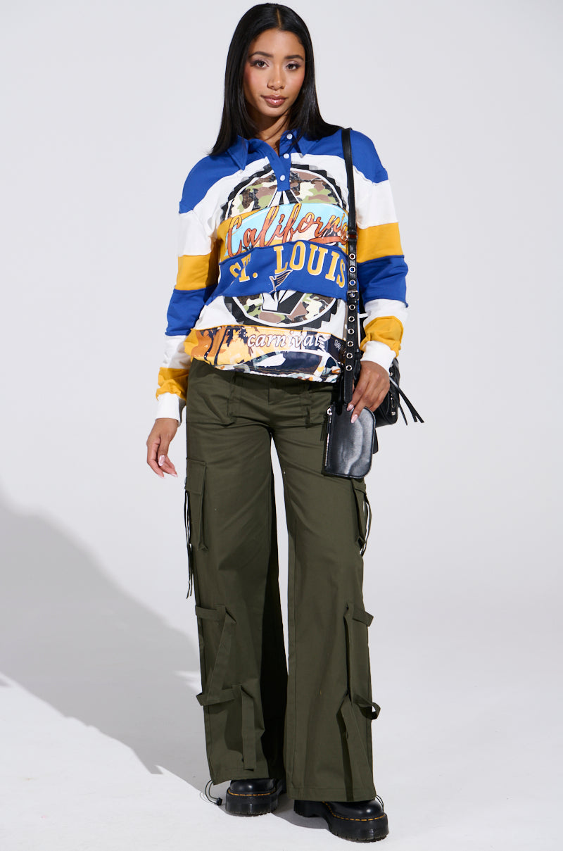 The individual confidently wears a colorful striped hoodie with a St. Louis graphic, olive IT IS BACK CARGO PANTS with drawstring hems, and black platform shoes. They're holding a black handbag with a chain strap, adding to the bold urban vibe.