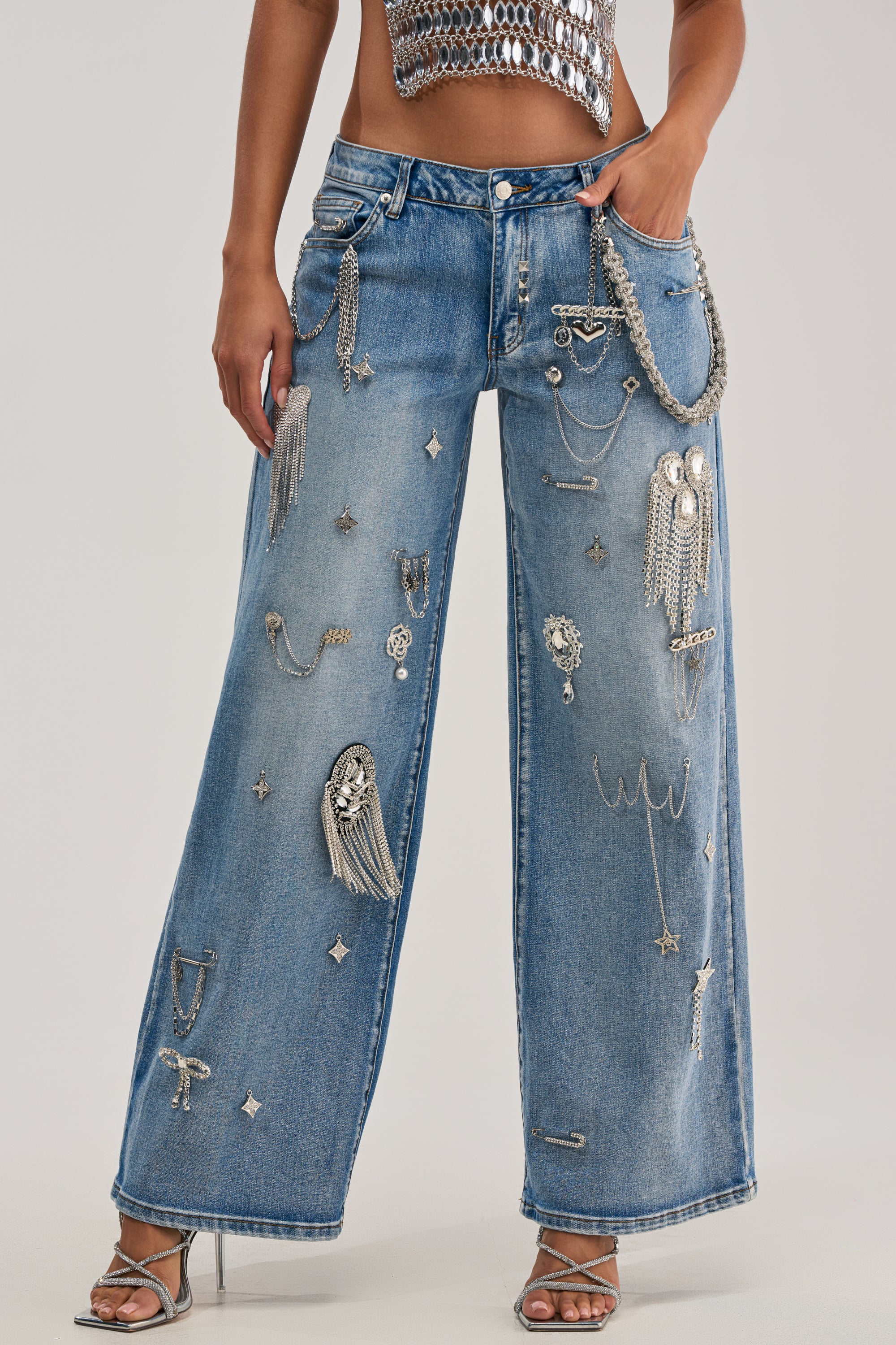 Wearing THE BEST ONE YET RELAXED FIT BLING DENIM JEANS with silver chains and jewels, styled with silver high-heeled sandals and a metallic crop top.