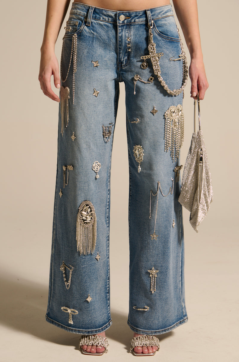 Dressed in THE BEST ONE YET RELAXED FIT BLING DENIM JEANS with silver chains and stars, they carry a sparkling handbag in their right hand and wear open-toed shoes with rhinestone details.
