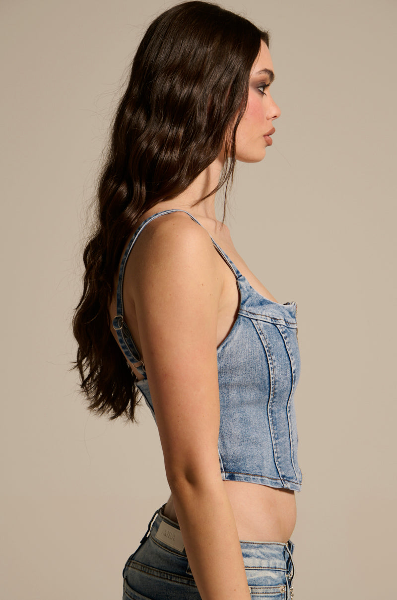 A woman with long, wavy brown hair is wearing THE BEST ONE YET DENIM CORSET with a metallic zipper and matching jeans. She faces left, highlighting her side profile against a plain background.