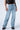 A person is modeling the EVERYTIME RHINESTONE EMBELLISHED STRAIGHT LEG JEANS in a high rise light blue wash, adorned with numerous small studs. They are also wearing a black leather vest and black leather shoes with studded details. The image is cropped at the waist and feet, focusing on the jeans.