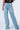 A person is shown from the waist down, wearing EVERYTIME RHINESTONE EMBELLISHED STRAIGHT LEG JEANS in light blue, featuring metallic studs. They are also wearing a black top. The loose-fitting jeans have visible back pockets and the person is standing against a plain, light background.