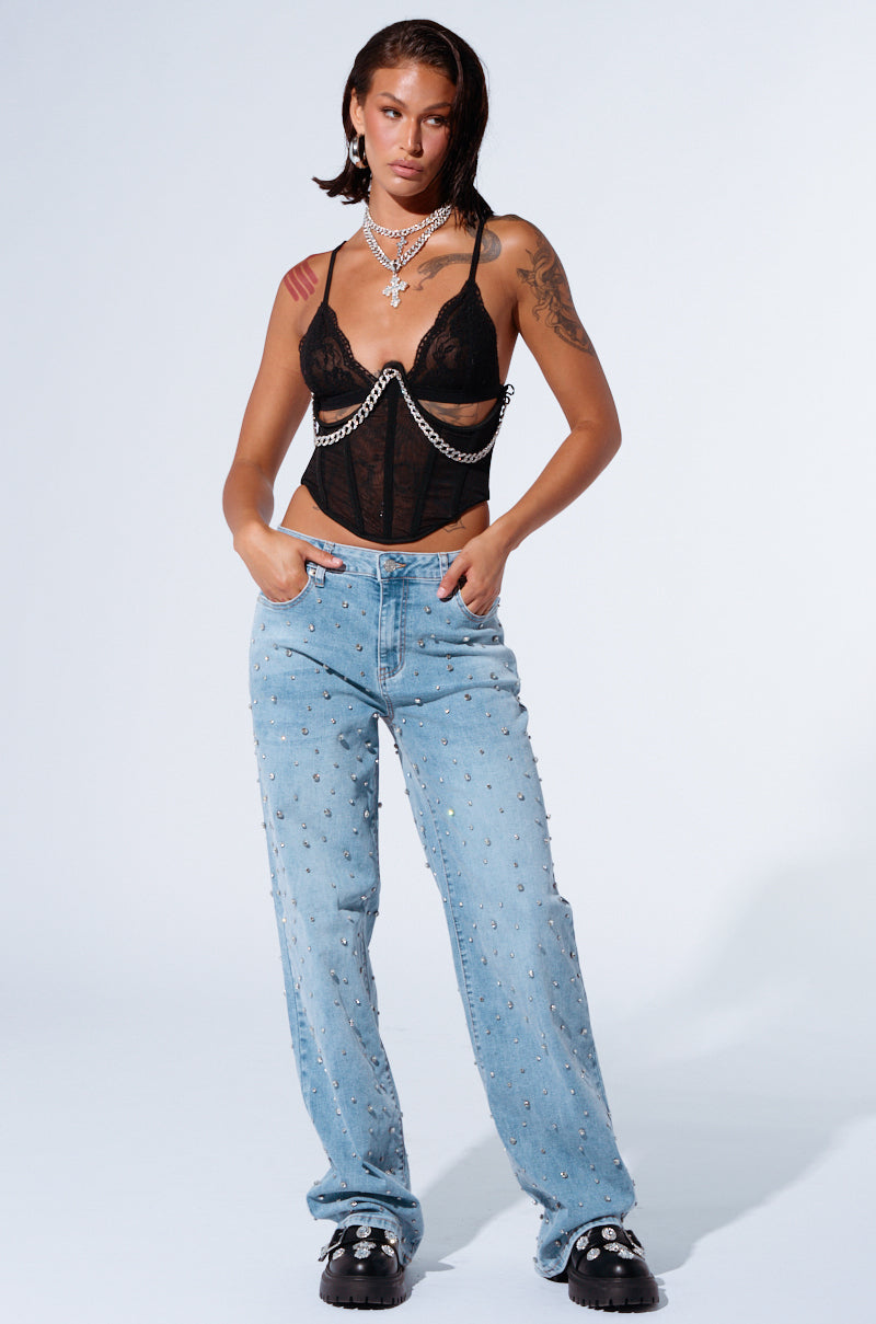 A person with wet-look shoulder-length hair, adorned in a black lacy top with chain accents, complemented by EVERYTIME RHINESTONE EMBELLISHED STRAIGHT LEG JEANS and chunky black shoes. Their ensemble is accessorized with multiple necklaces as they stand with their hands in their pockets against a plain background.