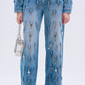 Wearing KEY TO THE CITY RELAXED FIT JEANS—inspired blue, mid-rise denim with metal key details—a person holds a small metallic chain purse and wears open-toed heels, all set against a plain white background.