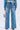 Someone is seen from the back wearing KEY TO THE CITY RELAXED FIT JEANS, featuring wide blue legs adorned with silver keys. They hold a small metallic purse against a plain, light-colored background.