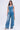 A woman in the AKIRA Label Key To The City Relaxed Fit Jeans, adorned with metal keys, stands against a plain background, holding a small silver handbag and wearing sunglasses and heeled sandals.