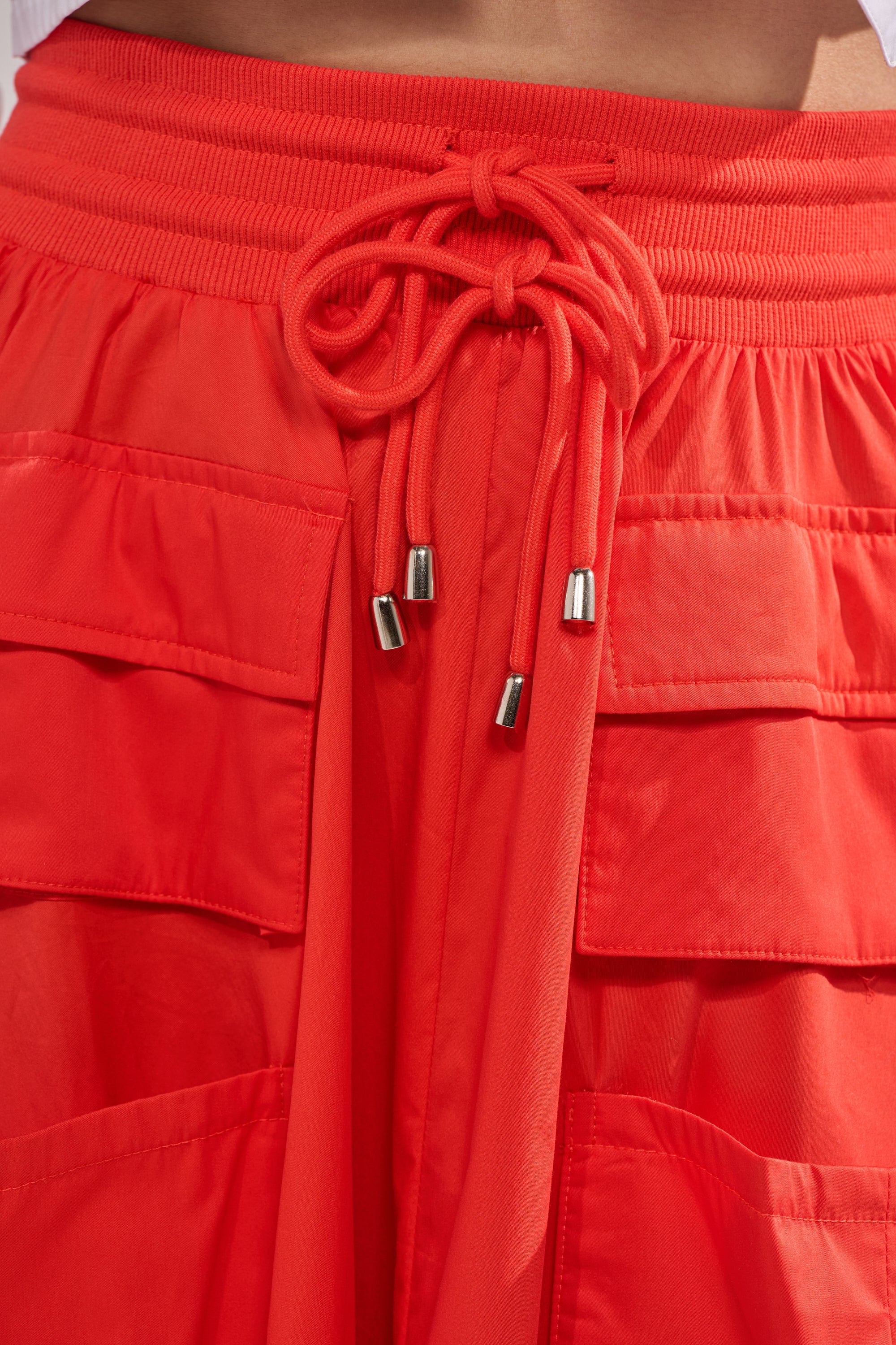 Close-up of the AMELIA CARGO POCKET MAXI SKIRT IN RED, featuring a stretchy waistband, metal-tipped drawstrings, and two large front cargo pockets. 6