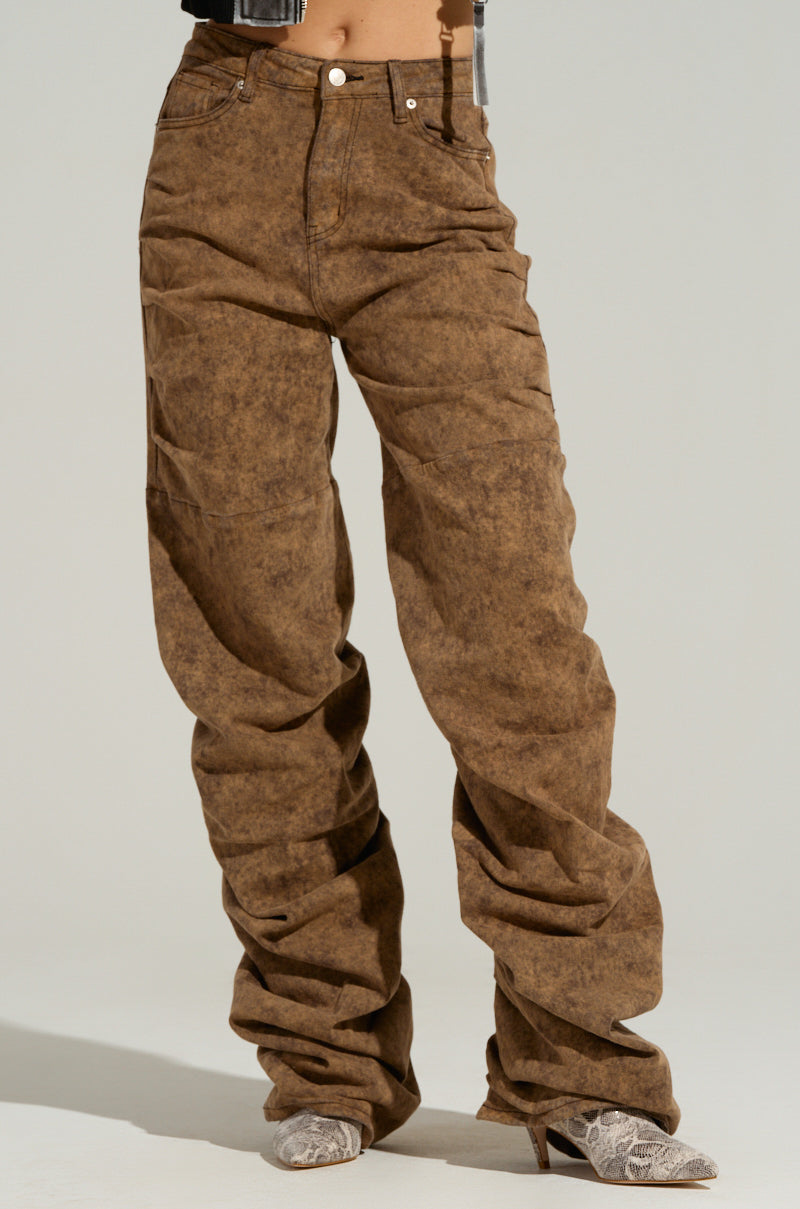 A person is wearing the NEVER CHANGE UP Corduroy Effect Ruched Pant, which are high-rise and loose-fitting brown jeans with distressed texture and ruched detailing around the lower legs. The pointed-toe, heeled shoes with a snakeskin pattern complement the look perfectly. The background is plain and light-colored, making the outfit stand out.