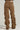 A pair of the NEVER CHANGE UP Corduroy Effect Ruched Pants viewed from the back, showcasing a distressed brown, baggy design with multiple horizontal ruched details along the legs. These high-rise jeans feature two back pockets and a leather patch on the waistband.