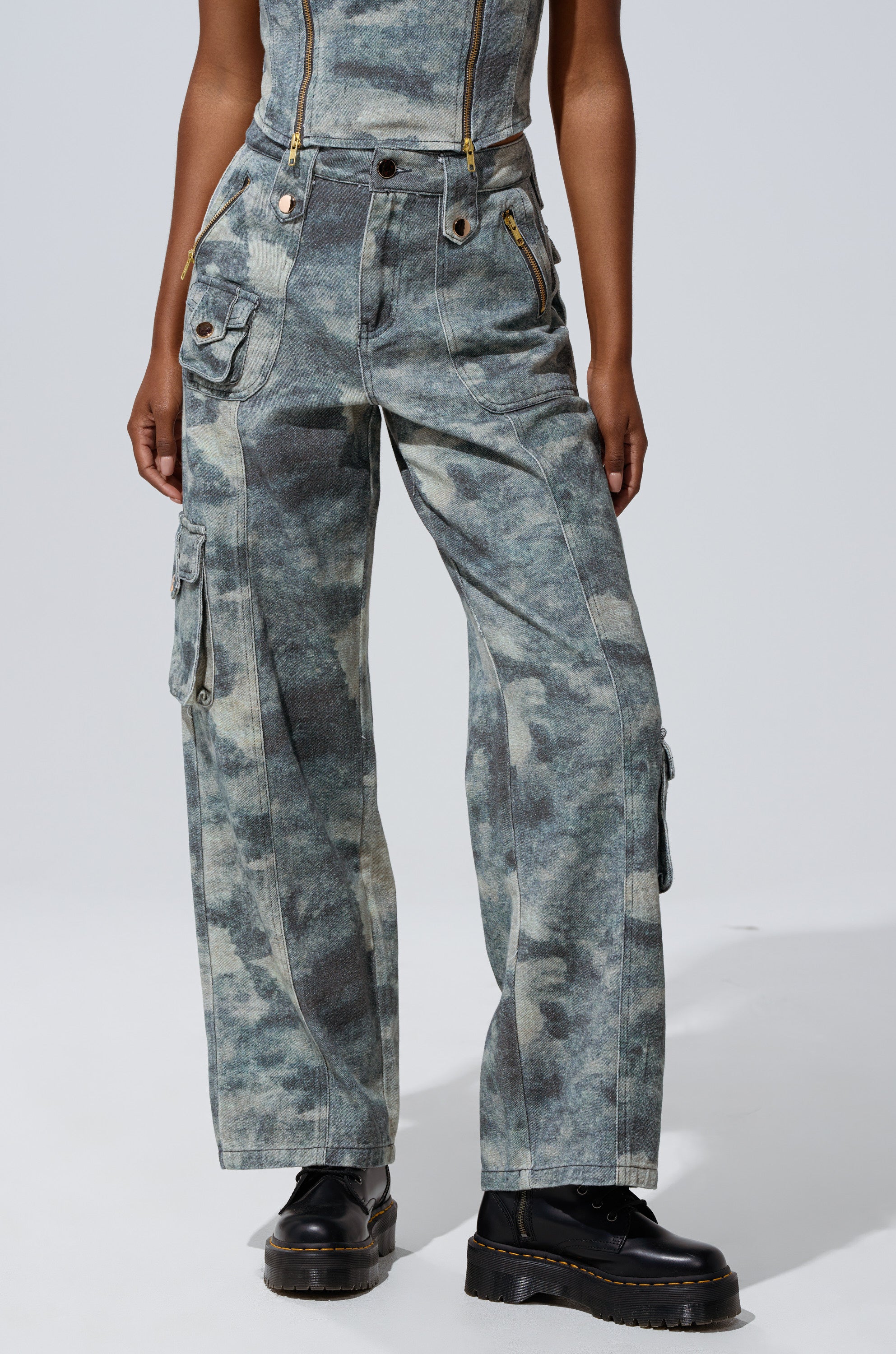 Model wears the STEPH CAMO DENIM RELAXED PANT—high-rise, wide-leg street style with visible zippers and pockets—paired with black platform boots against a plain light background. 2