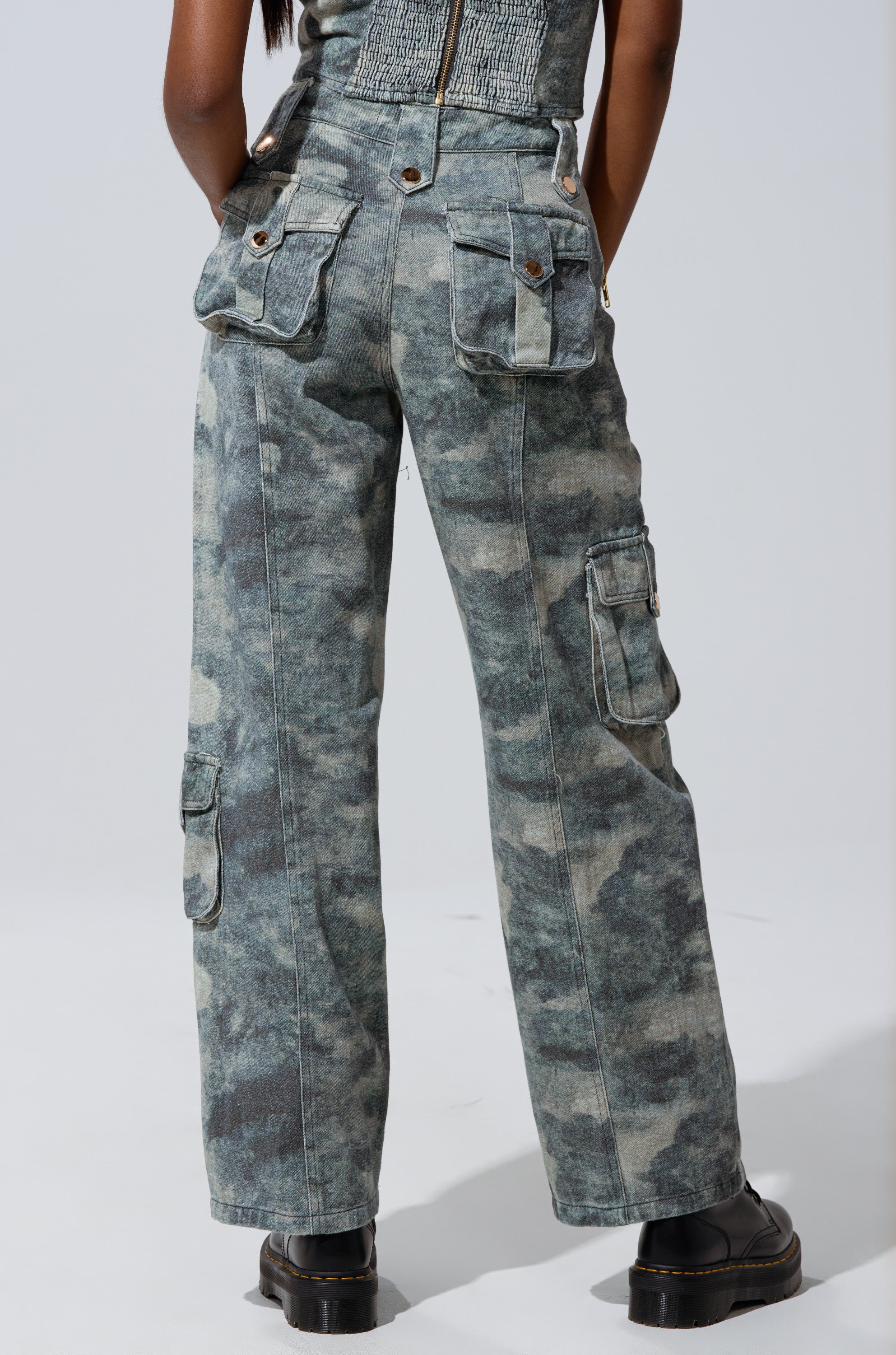 A person shown from the back wears STEPH CAMO DENIM RELAXED PANT—high-waisted green camo cargo pants with multiple pockets—paired with black boots, channeling high-rise street style against a plain white background. 5