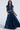 A woman dons an AKIRA Label blue denim cropped vest and a CARRIE ULTRA WIDE LEG DENIM TROUSER, confidently posing with her hand in her pocket against a minimalistic background. The high-rise design combines style with ease.