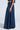 Someone is presenting the AKIRA Label ensemble with the CARRIE ULTRA WIDE LEG DENIM TROUSER, a long dark blue denim skirt featuring wide-leg elegance and practical pockets, standing sideways against a plain, light background.