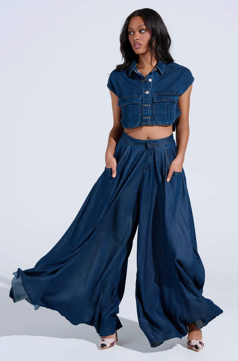 Against a plain light background, a woman models her chic style in a short-sleeved cropped dark wash denim jacket paired with CARRIE ULTRA WIDE LEG DENIM TROUSERS, hands in pockets.