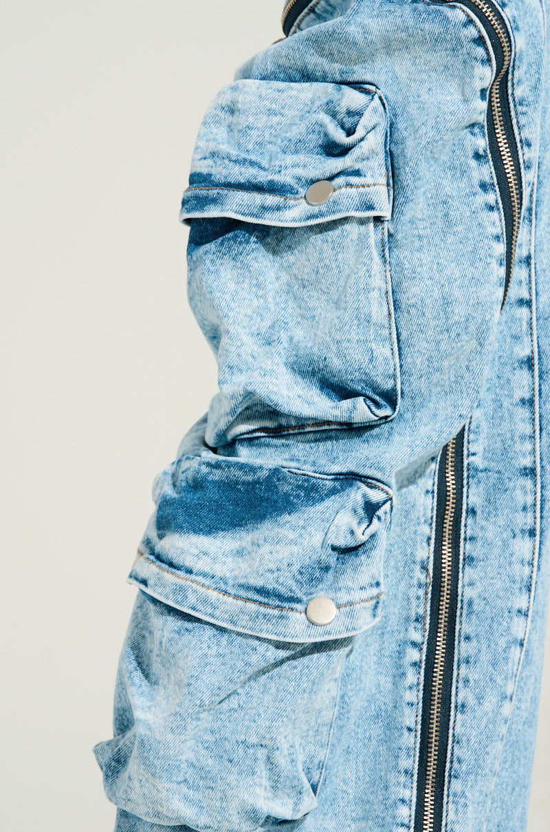 Close-up of a blue denim jacket with intricate stitching and zippers, echoing the style of POCKETFUL ZIPPER DENIM JEANS. The sleeve includes two folded flap pockets secured with buttons. The fabric presents a subtle worn, textured appearance, enhancing its casual vibe.