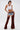 A woman poses against a white background wearing INCREDIBLE VELVET DENIM CHAPS over high heels, paired with a white crop tank top, layered necklaces, sunglasses, distressed denim mini shorts, and a western-style buckle belt.