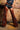Wearing the INCREDIBLE VELVET DENIM CHAPS over black leather shorts with a denim vest and high heels, someone poses before a rustic brick wall and wooden floor, capturing a bold, edgy Western-inspired style.
