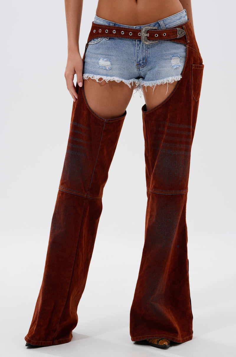 A person wears the INCREDIBLE VELVET DENIM CHAPS—distressed denim shorts with attached brown velvet chaps and a brown belt—for a bold cowgirl couture look that features exposed upper thighs.