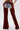 A person, shown from the back, wears INCREDIBLE VELVET DENIM CHAPS over frayed shorts. These chaps feature lace-up waist detailing, side zippers, and wide legs for a statement cowgirl couture look. The upper body is not visible.