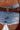 A close-up of someone wearing INCREDIBLE VELVET DENIM CHAPS with a distressed patch and a wide brown leather belt with a Western-style buckle, capturing true cowgirl couture.