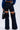 Wearing the LOCKED UP DENIM PANT—dark-wash wide-leg jeans with large thigh cutouts, exposed seams, and a mid-rise fit—paired with a blue top and a black handbag.
