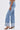 A person wearing the IN THE MOOD DENIM PANT, featuring high-rise straight legs and wide cuffed hems, paired with animal-print heeled sandals, shown from the side against a plain white background.