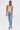 A woman with straight half-up hair walks confidently in a green floral-embroidered camisole, IN THE MOOD DENIM PANT with cuffed hems, and heeled sandals against a plain white background.