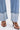 A close-up of a person wearing the IN THE MOOD DENIM PANT—light blue, high-rise, wide-leg jeans with a cuffed hem—paired with brown animal print high-heeled sandals, standing on a white surface.