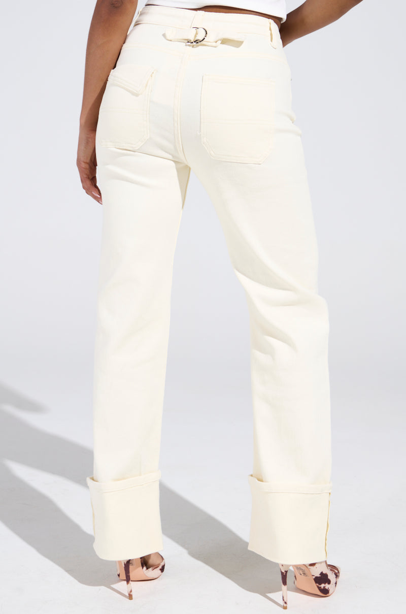 A person stands slightly angled in high-rise, semi-stretchy JUST GO WITH IT IVORY DENIM PANT with cuffed hems and visible back pockets. They pair the ivory jeans with a buckled belt and patterned high-heeled shoes.