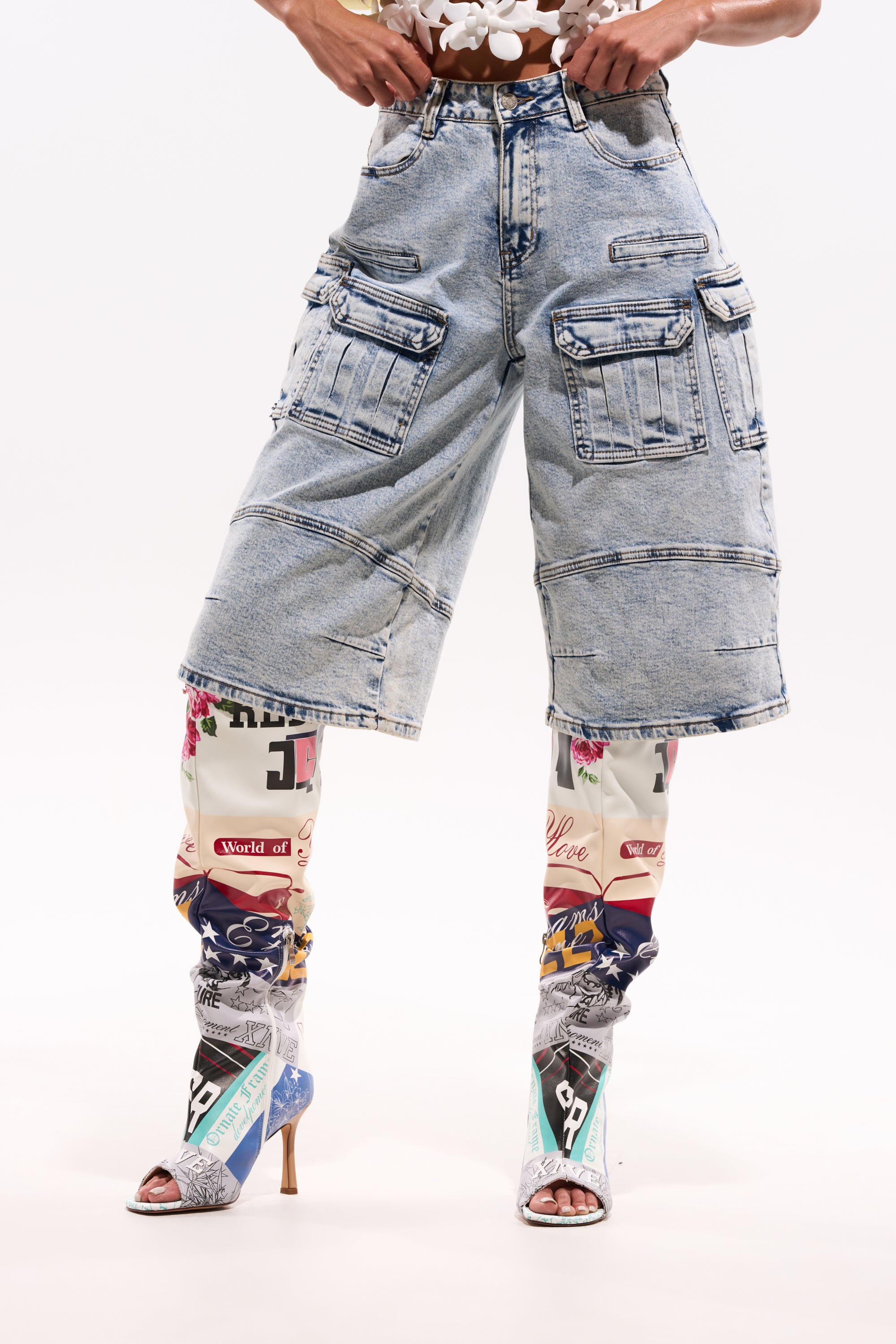 Someone wearing the FORGET ME NOT DENIM CARGO BERMUDA SHORT over vibrant graphic leggings and high-heeled open-toe shoes poses against a plain white background. 1