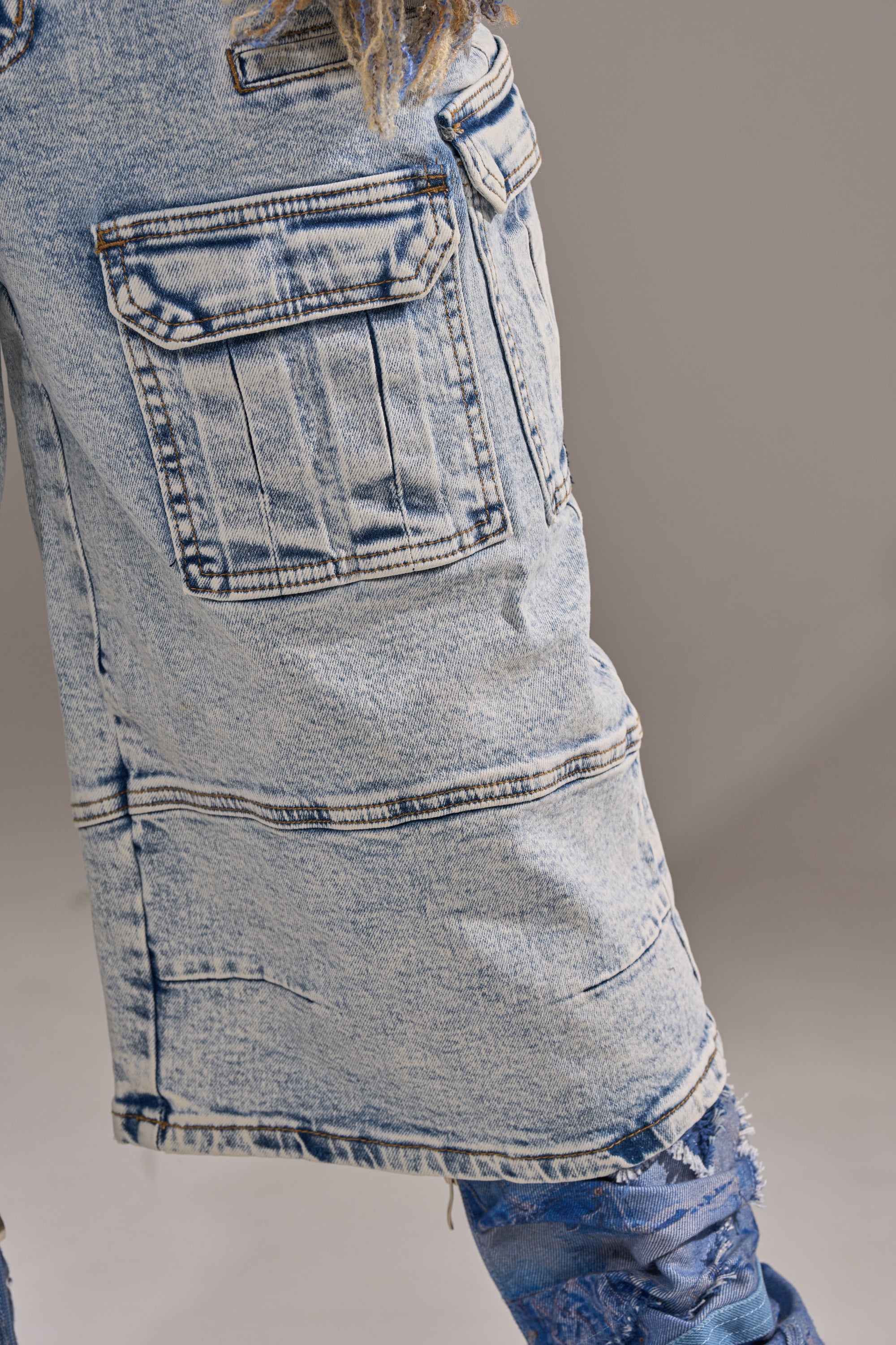 Close-up of a person wearing the FORGET ME NOT DENIM CARGO BERMUDA SHORT in light-wash denim, featuring large pockets and visible seams, shown waist to above the knee against a neutral background. 11