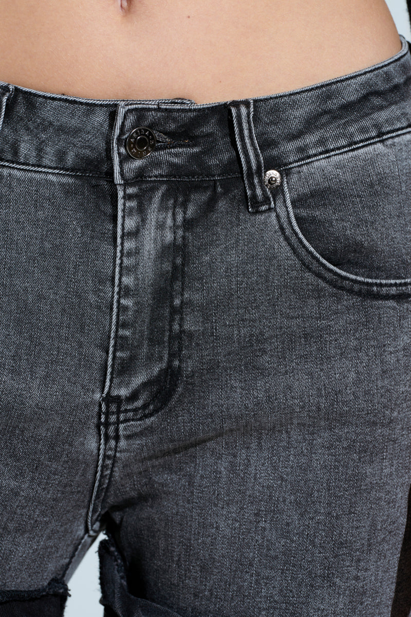 Close-up of a person in OH YEAH BABY black wash denim pants. These relaxed mid-rise jeans have button and zipper closure, slightly frayed near the thigh, with an upper waist and pockets set against a light background.