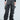 Wearing the "OH YEAH BABY BLACK WASH DENIM PANT," a person in relaxed mid-rise black denim stands against a plain background, pairing them with a black cropped top and accessorizing with a small silver handbag and open-toed black heels.