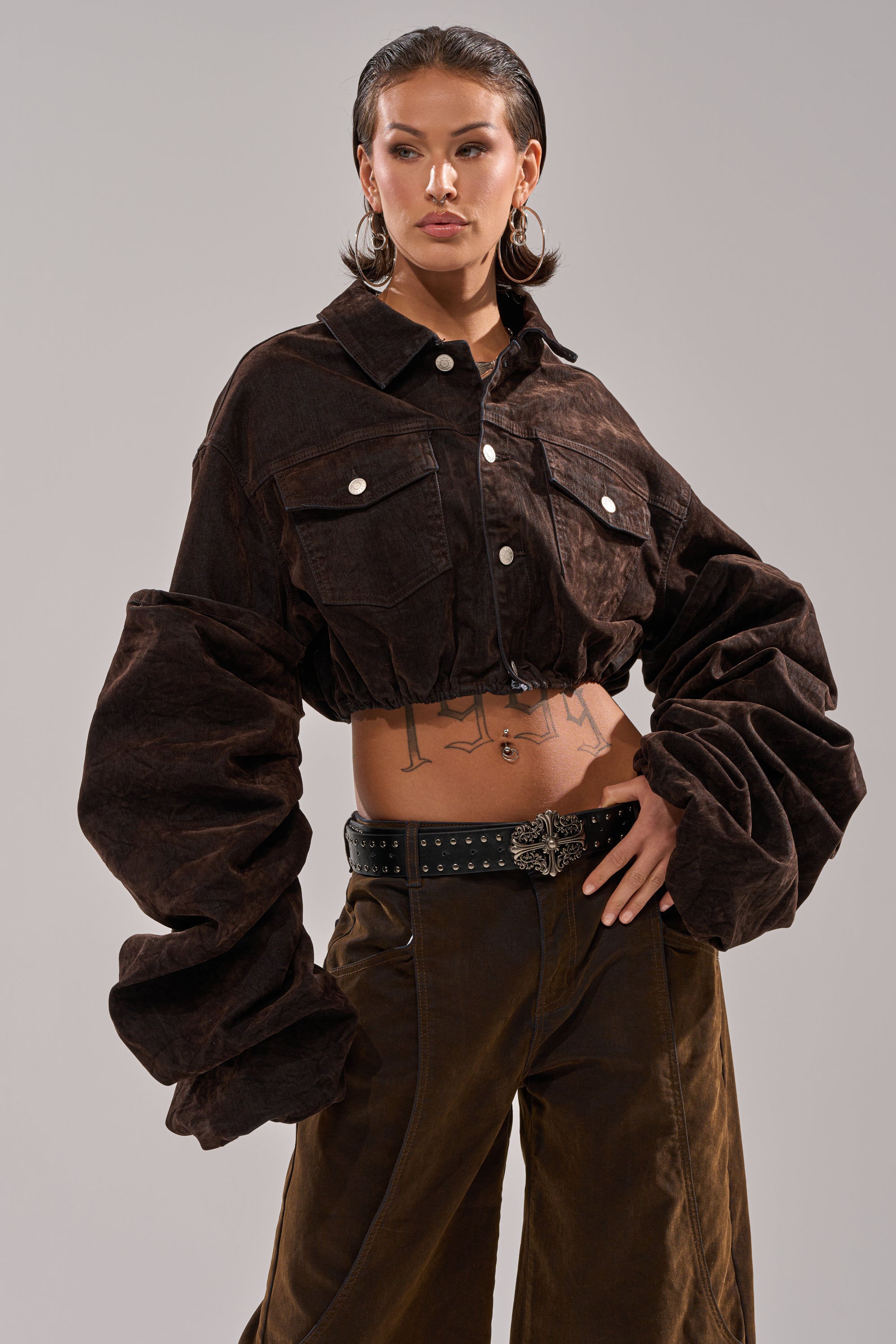 Wearing the STACKED SLEEVE VELVET DENIM JACKET with wide-leg pants, large hoop earrings, and a decorative buckle belt, a person poses confidently with one hand on their hip against a plain background.
