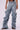 Someone is wearing the OH YEAH BABY DENIM PANT by JCR Trading LTD, featuring highly ruched, baggy light blue denim with a mid-rise waist. They stand against a plain white background with their hands resting at their sides. The jeans showcase exaggerated, dramatic folds and are paired casually with sandals.