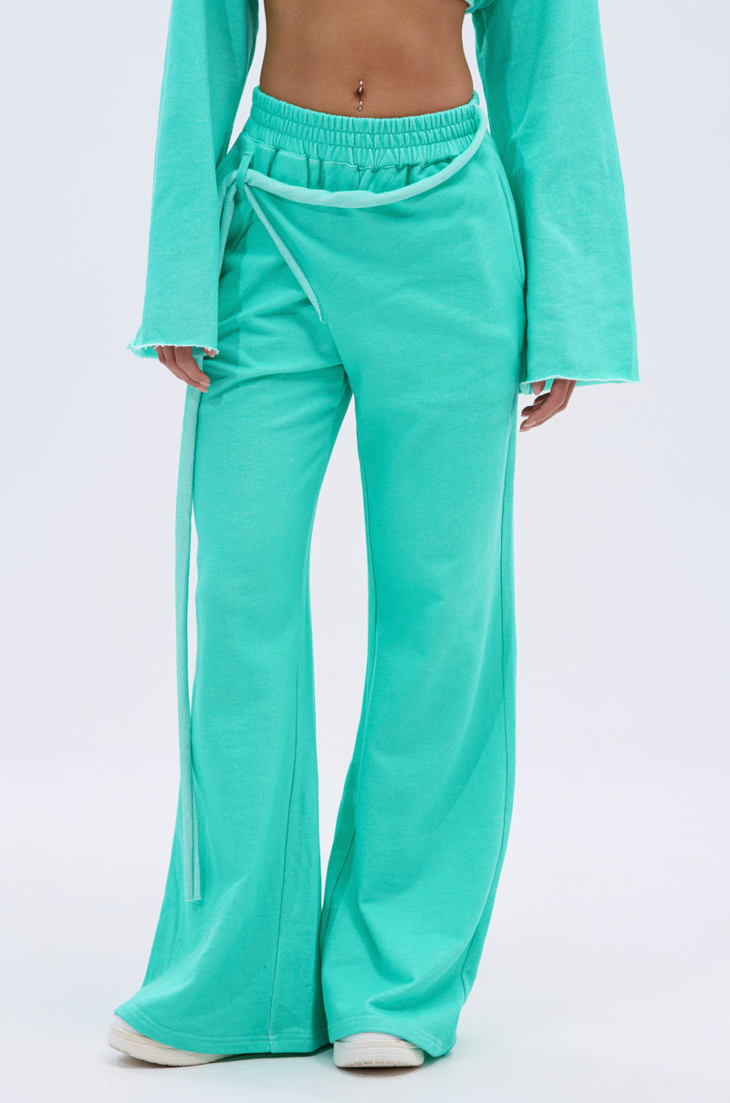 A person wears loose, bright turquoise ISSA JOGGER PANT IN TIFFANY with wraparound tie detail and a matching long-sleeve top; only the midriff to feet is visible. 1
