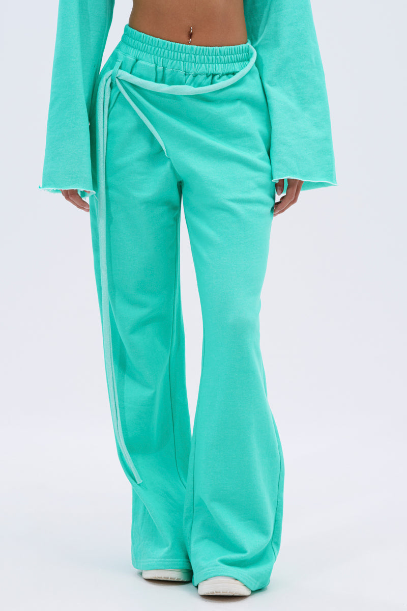 Person wearing the ISSA JOGGER PANT IN TIFFANY—aqua green, high-rise wide-leg joggers with a wrap tie detail—paired with a matching flared-sleeve top. Only the lower torso and legs are visible, showcasing the pant’s relaxed, casual style. 2